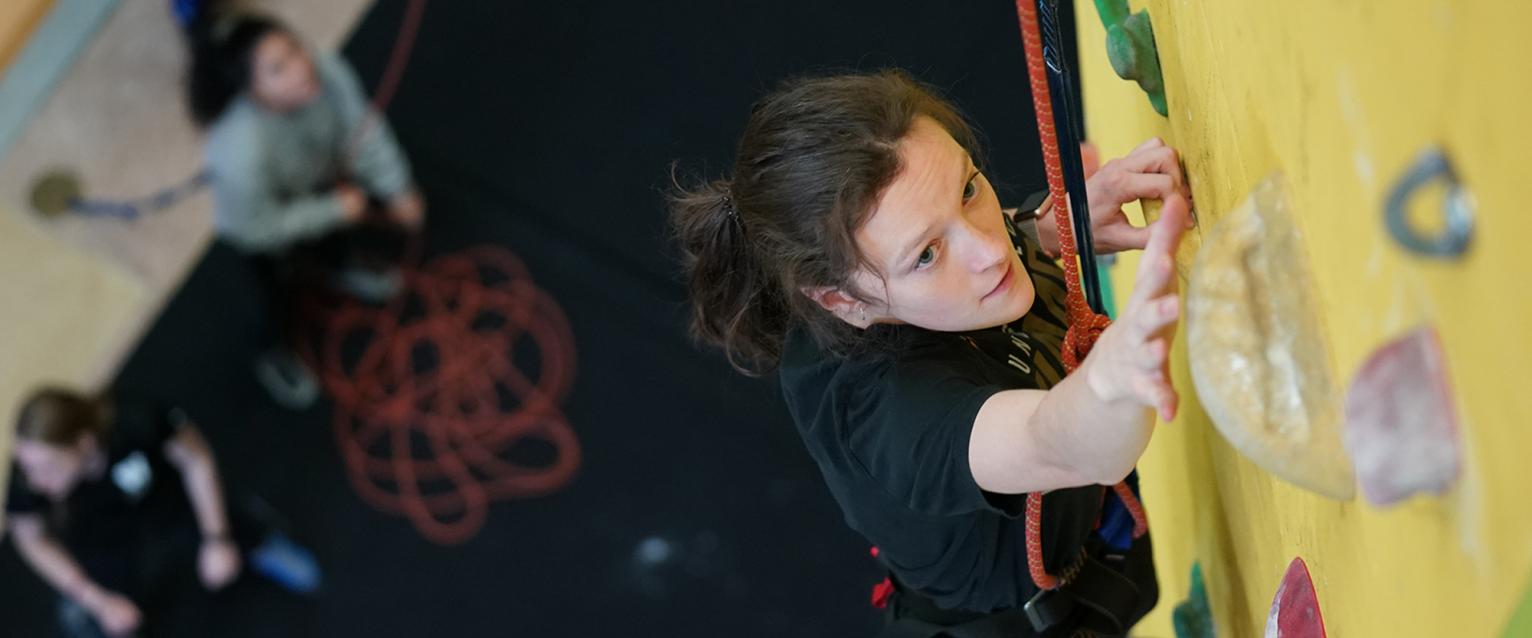 We create a connected community for students to thrive. A student on the climbing wall at the rec center, students looking up.